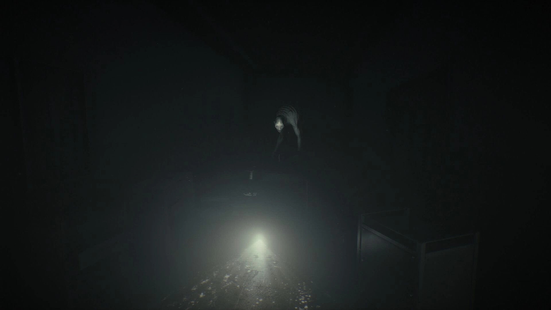 Unlisted: Pale figure crouches in a foggy hallway lit by a flashlight beam, crates nearby.