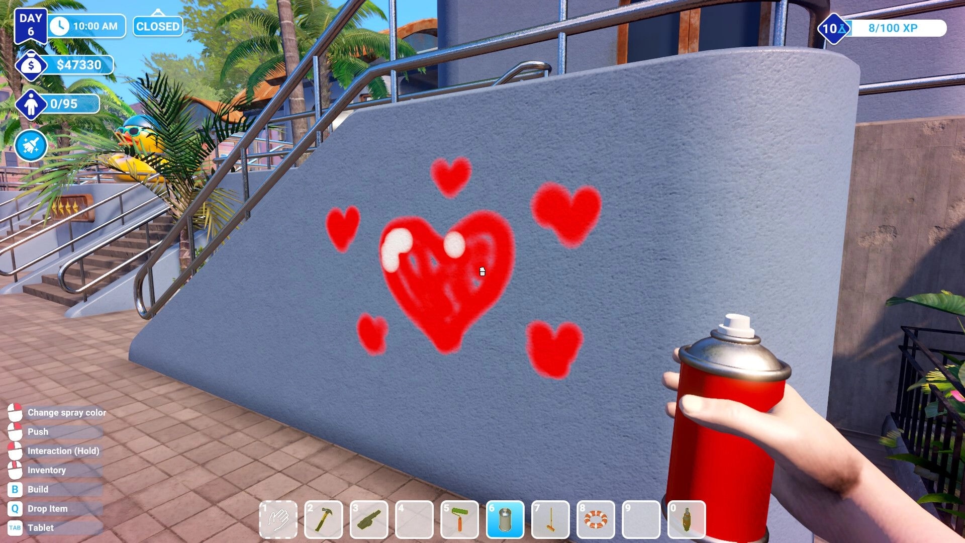 Waterpark Simulator: Player spray-paints red hearts on a wall beside stairs in a tropical park setting