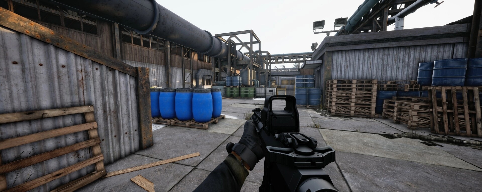 WRAITH OPS: First-person view aiming gun in industrial area with blue barrels and wooden pallets