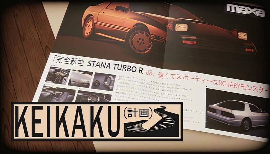 Keikaku計画: close-up of a magazine page featuring a red sports coupe photo on a desk under warm lighting.
